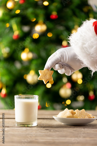 Image of hand of santa claus holding christmas star biscuit over glass of milk