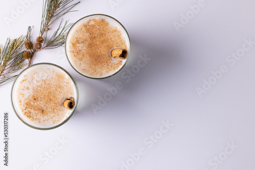 Image of two glasses of milk with cinnamon sticks christmas decorations copy space on white