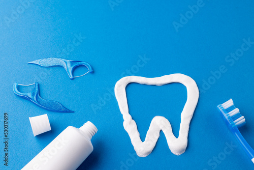 Image of toothbrush, toothpaste, strings and tooth made of paste on blue surface