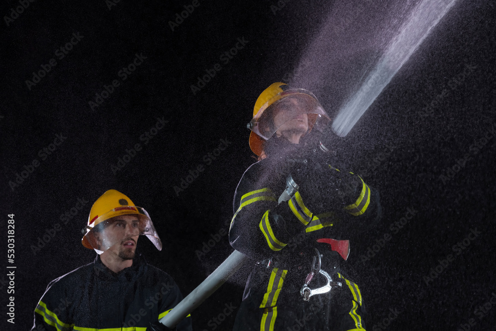 Fototapeta premium Firefighters using a water hose to eliminate a fire hazard. Team of female and male firemen in dangerous rescue mission. 
