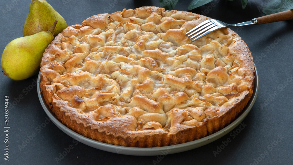homemade pear pie on a black background in a gray plate with pears and fork