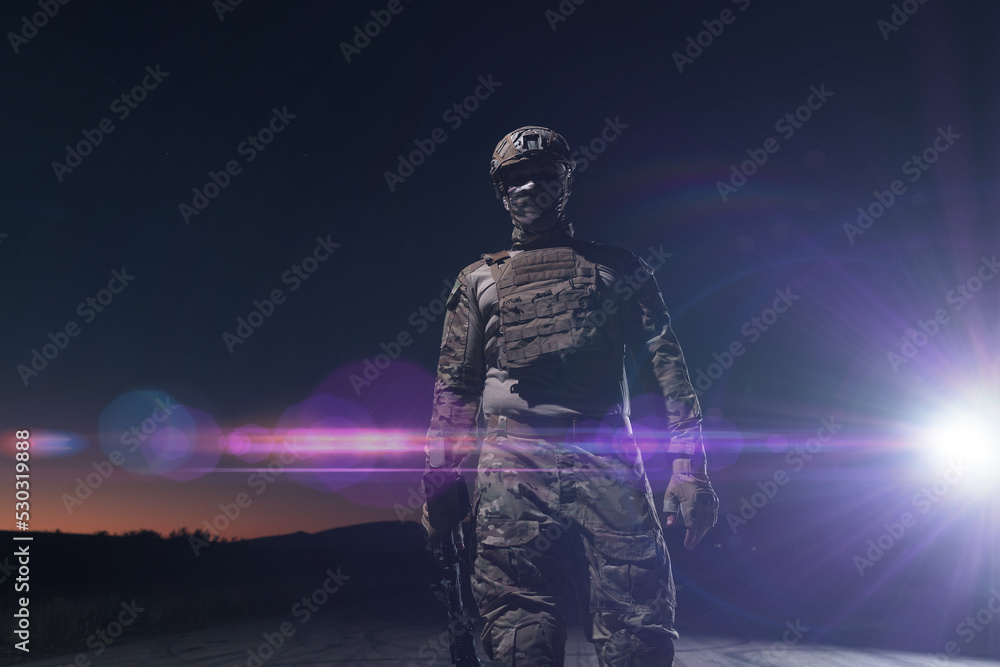 Fototapeta premium Army soldier in Combat Uniforms with an assault rifle, plate carrier and combat helmet going on a dangerous mission on a rainy night. 