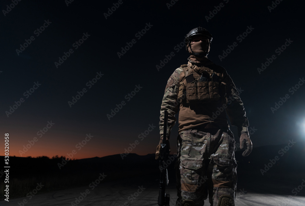 Army soldier in Combat Uniforms with an assault rifle, plate carrier and combat helmet going on a dangerous mission on a rainy night. 