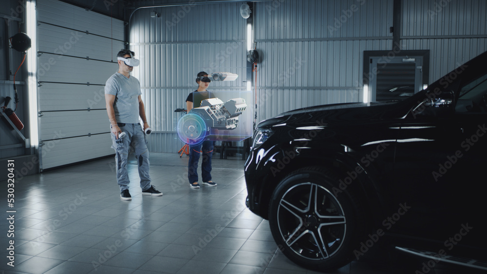 Two technicians check a car engine using virtual reality technology in a workshop. Experts discuss the characteristics of the motor of the car, its components and parts Two technicians check a car engine using virtual reality technology in a workshop. Experts discuss the characteristics of the motor of the car, its components and parts