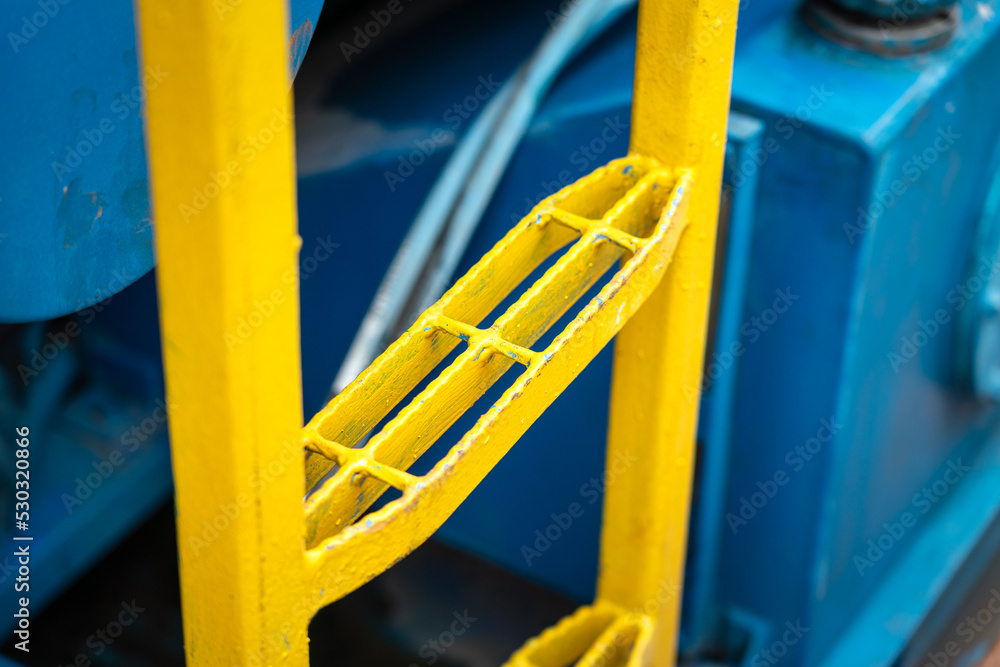 Metal fixed ladder of the construction working platform with safety anti-slip plate. Industrial equipment object photo, close-up and selective focus.