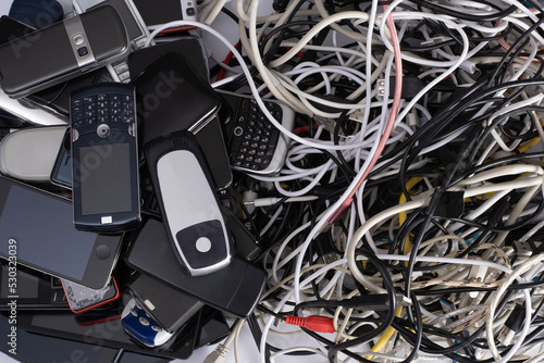 Pile of tangled old smart technology wires, charging cables and used obsolete mobile phones. Old electronic devices. The concept of recycling and disposal of electronic waste.