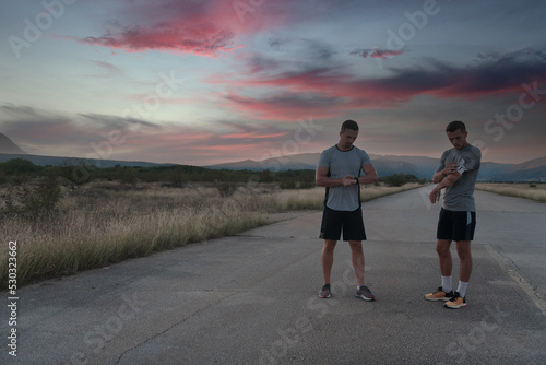 Sport couple looking at a smartwatch while standing on the country road. Resting after jogging and running exercise and checking heart rate and pulse.