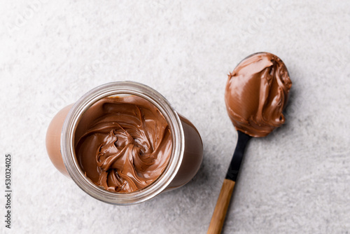 Image of spoon and jar with chocolate cream on light grey background