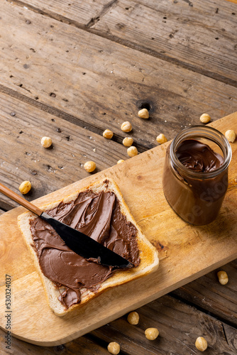 Vertical image of chocolate cream in jar and bread on wooden board and surface