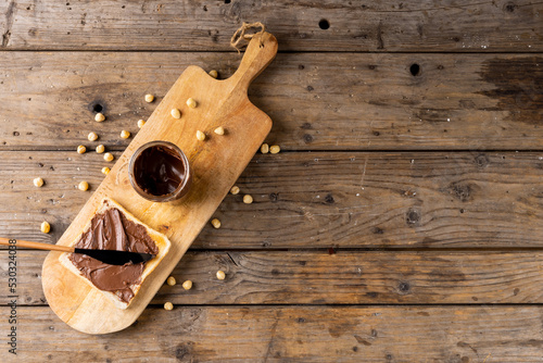 Image of chocolate cream in jar and bread on wooden board and surface