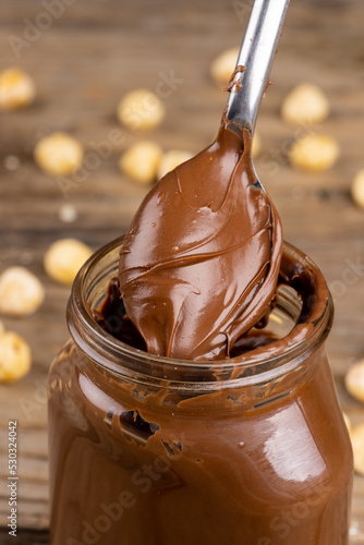 Vertical image of spoon with chocolate cream and nuts on wooden surface