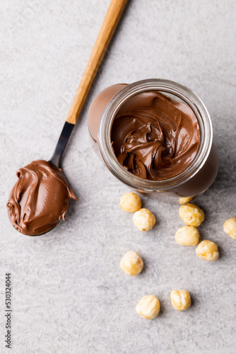 Vertical image of spoon with chocolate cream, jar and nuts on grey surface