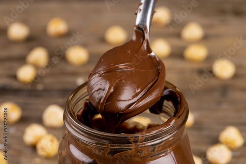 Image of spoon with chocolate cream and nuts on wooden surface