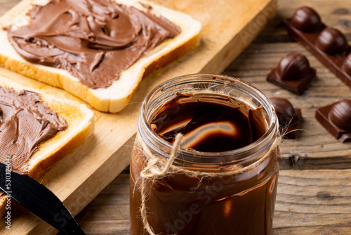 Image of chocolate cream in jar and bread on wooden surface