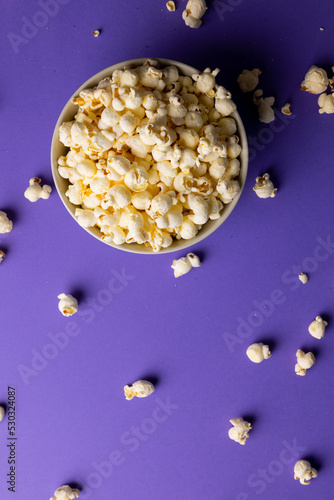 Vertical image of pop corn in bowl lying on violet background