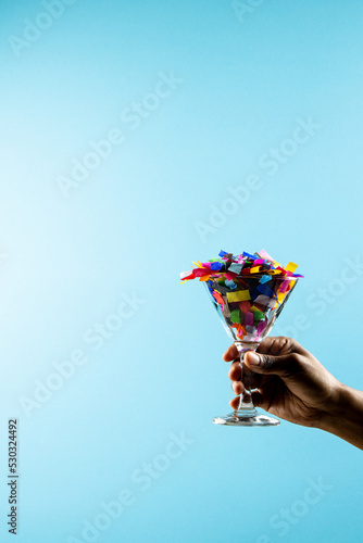 Composition of close up of hand with new years drink with confetti on blue background