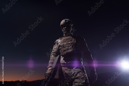 Army soldier in Combat Uniforms with an assault rifle, plate carrier and combat helmet going on a dangerous mission on a rainy night. 