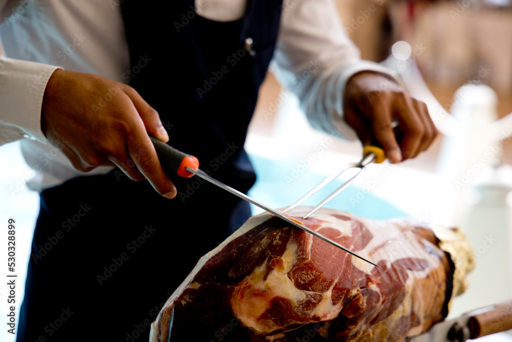 man's hands cutting raw ham with a tip of a shredder
