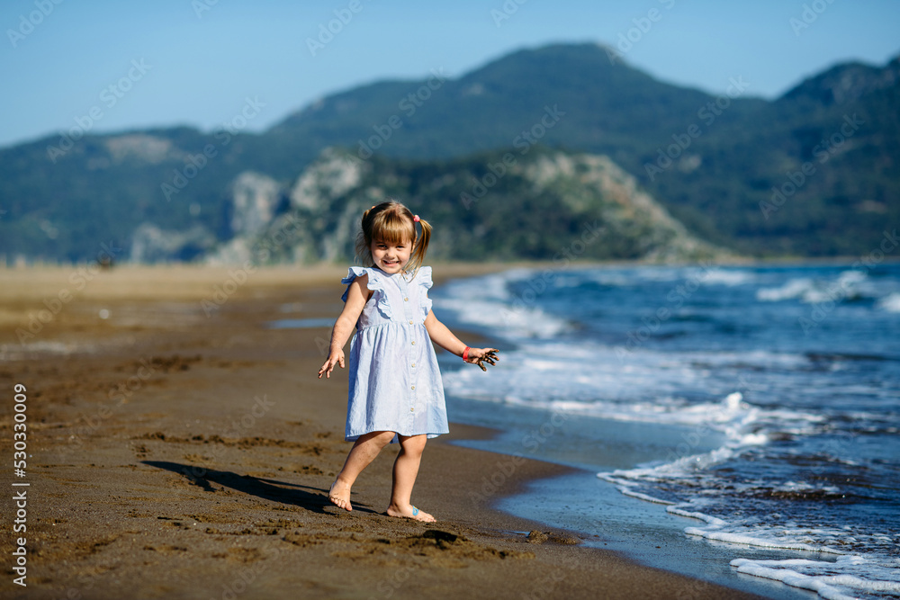 Cute little toddler girl in blue dress runnig and playing on the wild Iztuzu beach, Turkey