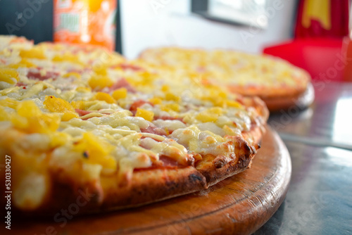 Pizza hawaiana con queso y crujiente en una base de madera con un fondo de restaurante 