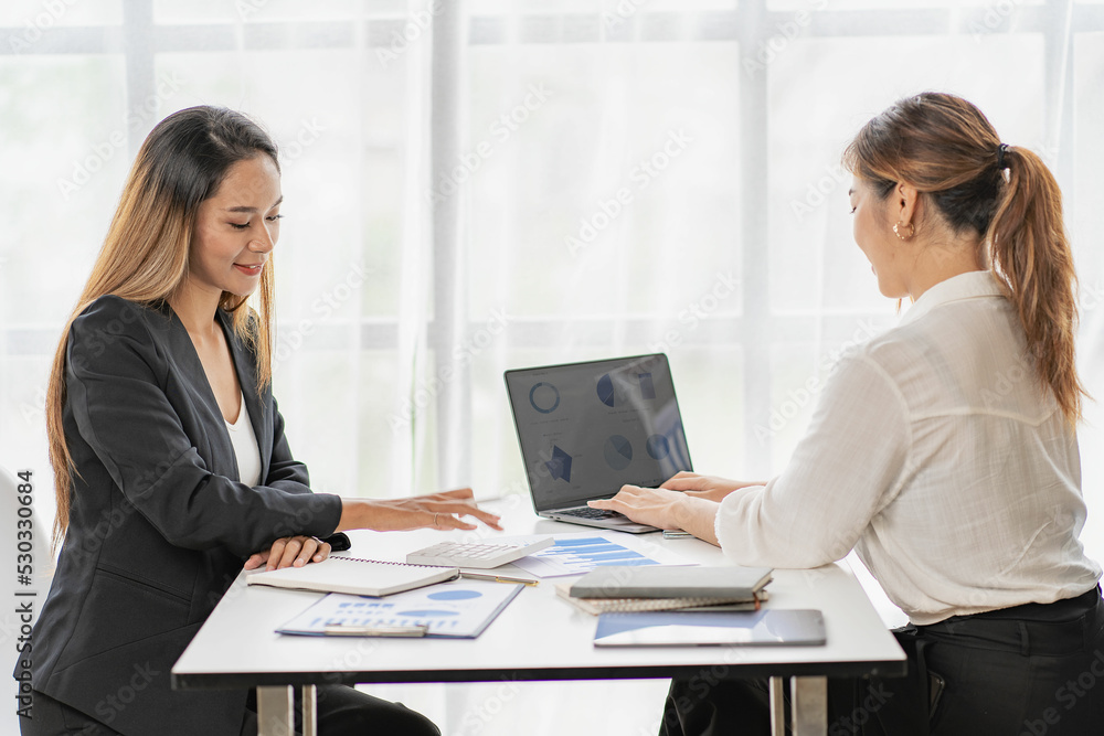 A team of Asian businesswomen discussing something and smiling as they sit at a desk in the office of women working together analyzing finances. A team of Asian businesswomen discussing something and smiling as they sit at a desk in the office of women working together analyzing finances.