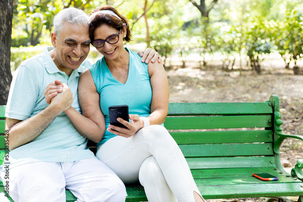 Fototapeta premium couple sitting on bench in park using phone