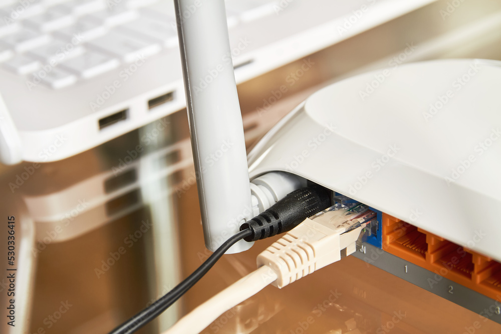White wireless wi-fi router near a laptop on a glass table White wireless wi-fi router near a laptop on a glass table