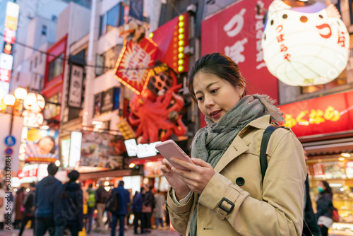 Asian Japanese girl tourist looking at online restaurant reviews on phone while deciding what to eat for dinner on lively Shinsaibashisuji shopping Street in Osaka japan