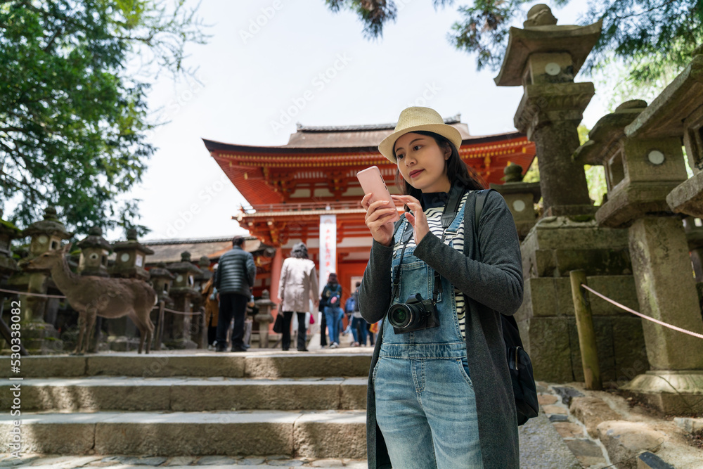 Asian Japanese girl backpacker consulting online travel info on mobile phone near a stone staircase while visiting kasuga taisha Shinto shrine in nara japan