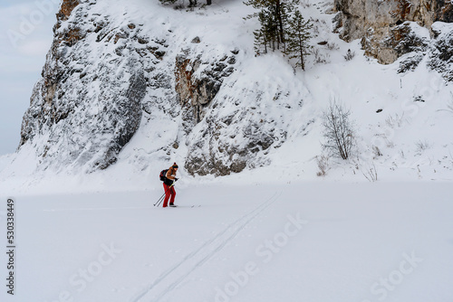 side view of young man in red brown clothes with backpack skiing near rocks and cliffs covered snow Active healthy lifestyle Winter sports Hiking