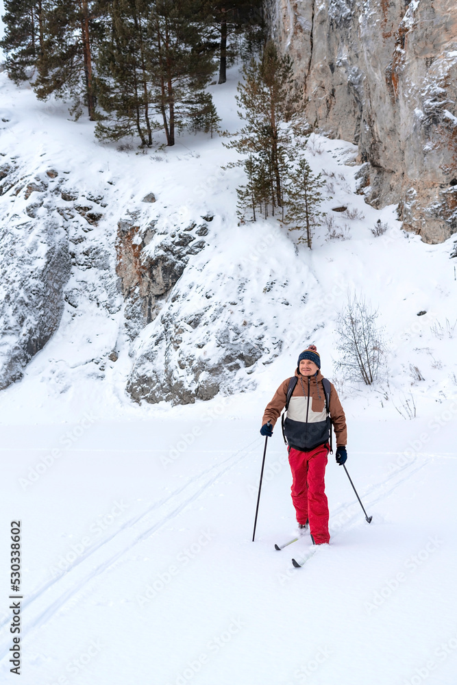 young man in red brown clothes with backpack skiing near rocks and cliffs covered snow Active healthy lifestyle Winter sports Hiking