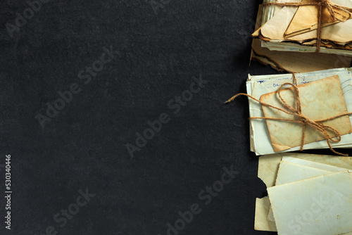 Stack of old torn vintage letters on yellowed paper against black granite table. © Loraliu
