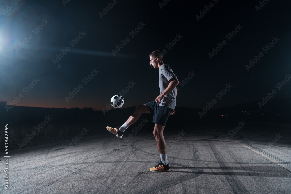portrait of a young handsome soccer player man on a street playing with a football ball.