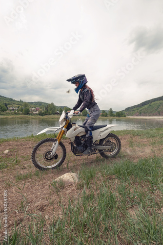 Beautiful female wearing helmet and moto protection turtle driving dirt motorcycle near the river