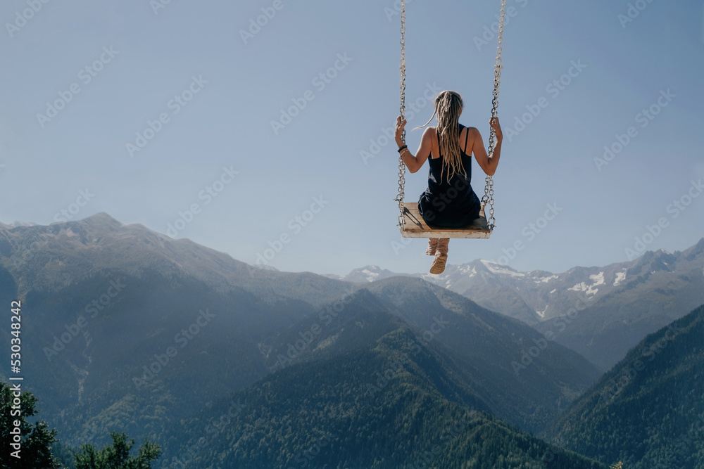 Young woman flying on swing in the sky over beautiful mountains, dream concept