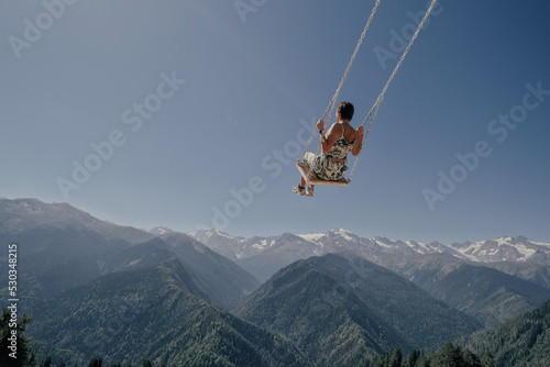  travel concept, Young beautiful woman flying on swing in blue sky over dizzying mountain gorge