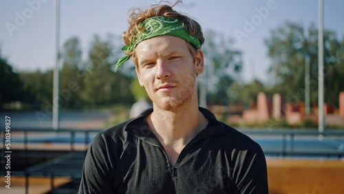 Curly-haired man with green headband looks in camera smiling photo