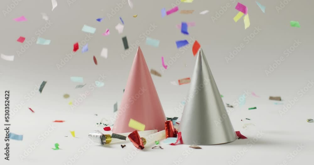 Video of a pink and a silver party hat with colourful confetti falling on pale grey background Video of a pink and a silver party hat with colourful confetti falling on pale grey background