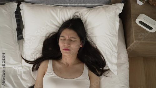 top angle shot with zoom in frightened asian female awaking from nightmare and catching her breath while looking upward on bed in the bedroom at home