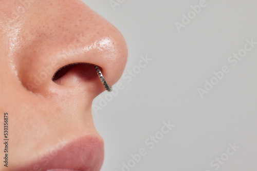 Closeup of a young woman's visage with piercing septum hanging from her nose.