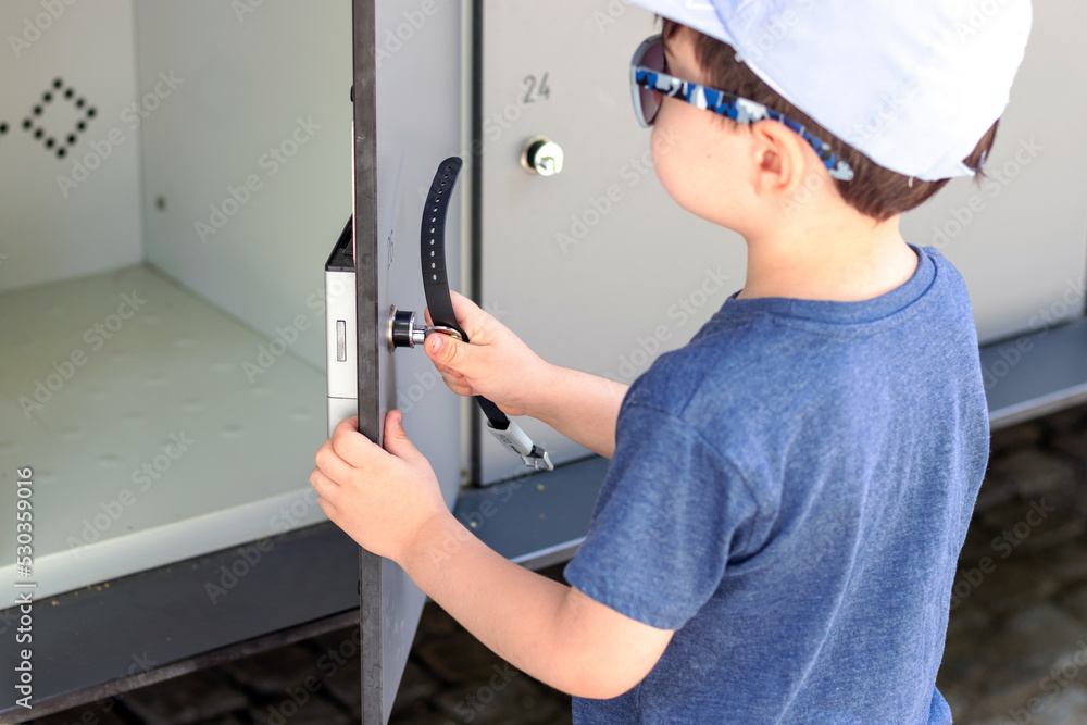 kid try to lock metal cabinet for keeping things.gray metal door with key.organizer for bags shoes clothes,steel locker for office gym market school or bank.numbers engraved on doors.back view closeup