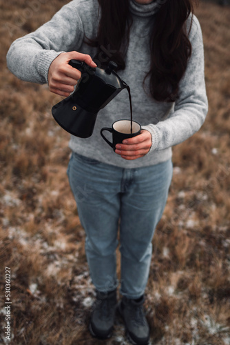 Close up of a woman pouring out coffee from Moka pot into a cup outdoors