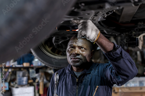 African auto mechanic fixing underneath vehicle in auto repair service shop, black man working in car garage , Car maintenance concept