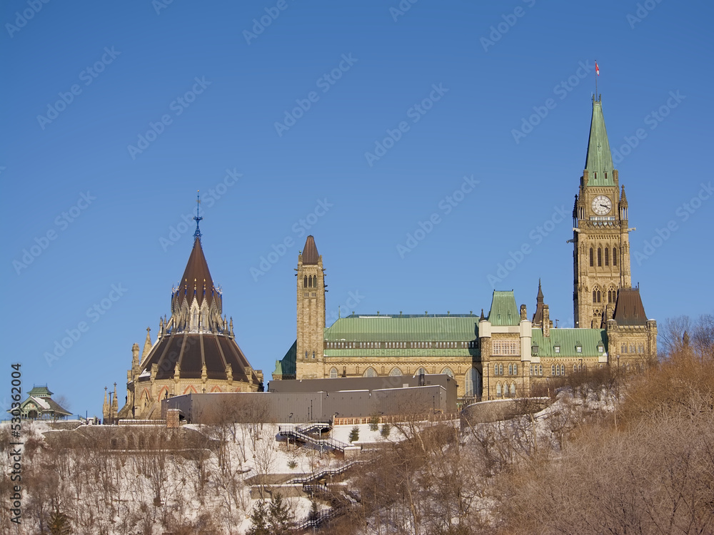 Gothic revival buildings and towers of parliament hill, seen from the park along Ottawa river on a sunny witer day with clear blue sky. Ontario, Canada 