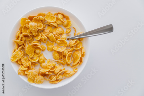top view of crispy corn flakes in bowl with spoon and milk isolated on white. photo