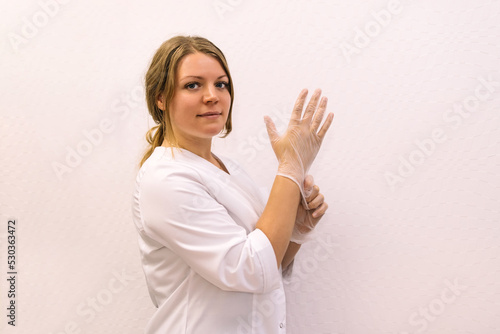 Portrait of cosmetologist in white gloves, portrait closeup view. Young woman beautician in her cabinet in white uniform before making face massage.