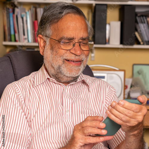 A senior man of Asian origin scrolloijg at his cell phone messages and smiling