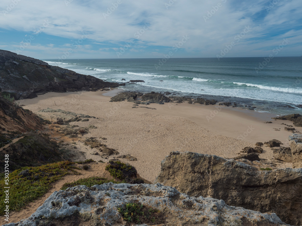 View of empty small sand beach with ocean waves and sharp rock and cllifs at wild Rota Vicentina coast near Porto Covo, Portugal. View of empty small sand beach with ocean waves and sharp rock and cllifs at wild Rota Vicentina coast near Porto Covo, Portugal.