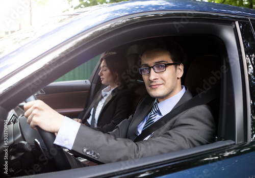 Handsome and confident businessman in black suit and his female colleague driving in luxury car  © Vitaliy