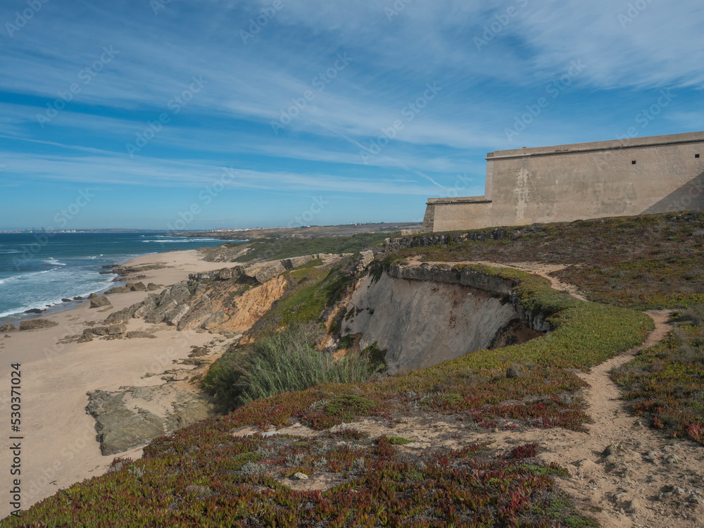 View of wall of fortress at Praia da Ilha do Pessegueiro sand beach with ocean waves at Rota Vicentina coast near Porto Covo, Portugal.